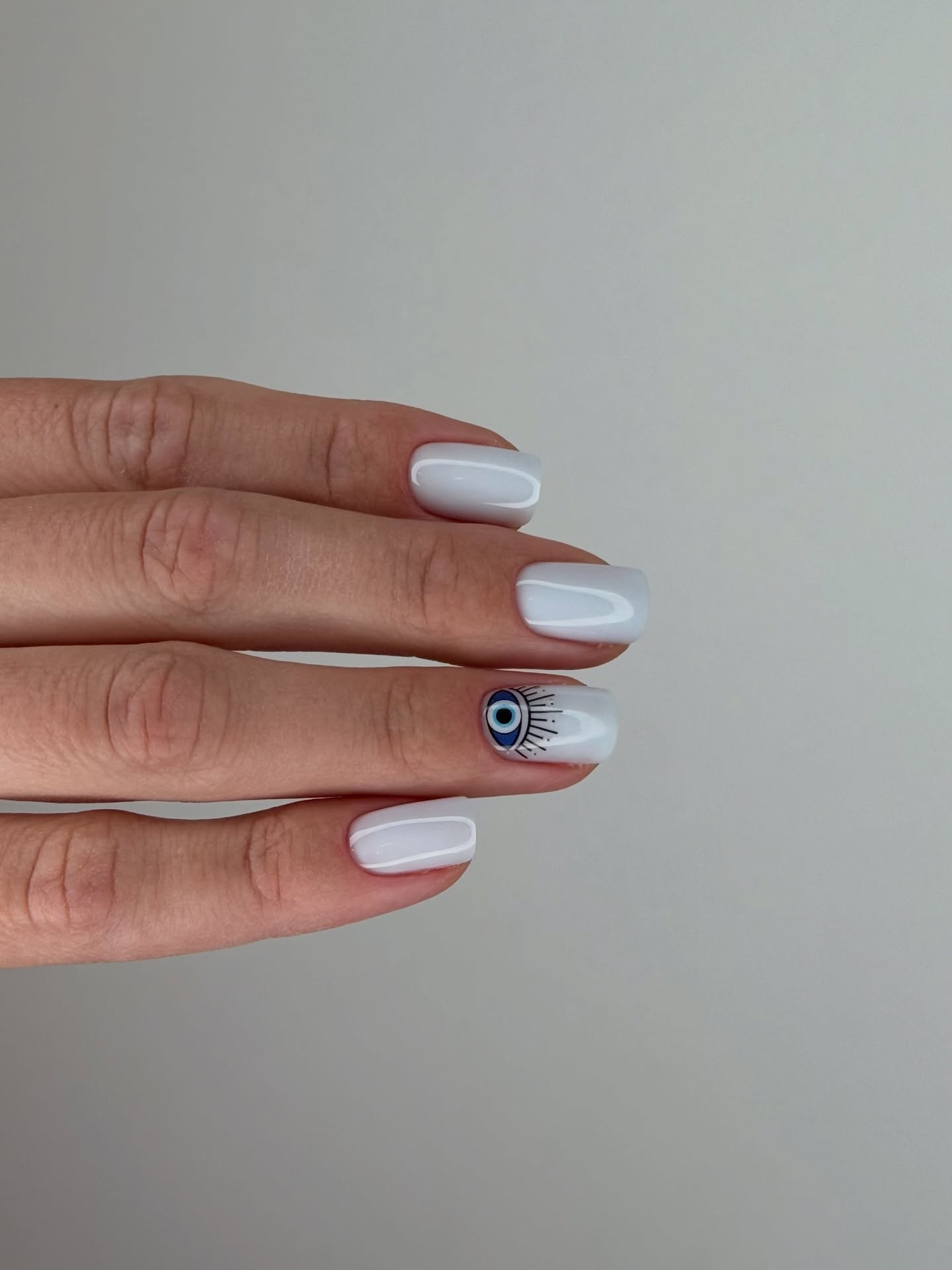 Witte nagels met een boze-oog-design op één nagel